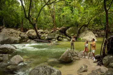 An Indigenous tour guide stood on a rock in the rainforest, alongside two visitors.